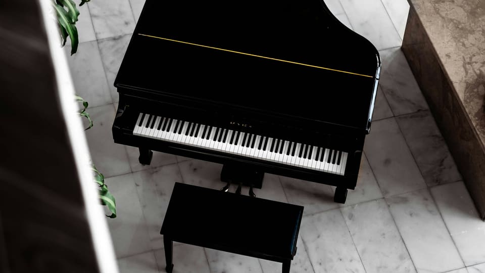 A black grand piano and bench seen from above on a marble floor