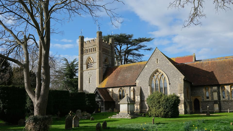 A stone church with a square tower behind trees