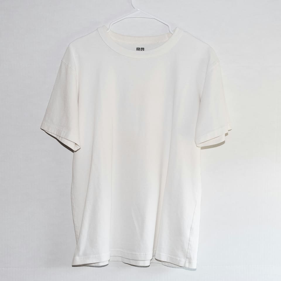 A plain white T-shirt hanging on a white wall