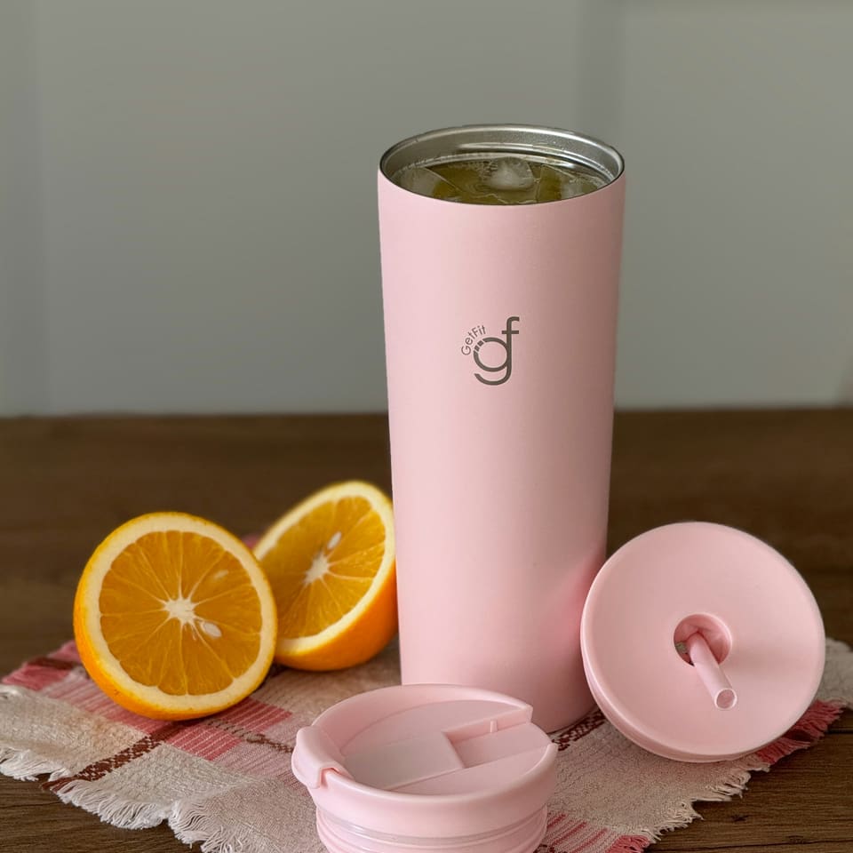 A pink tumbler beside sliced oranges